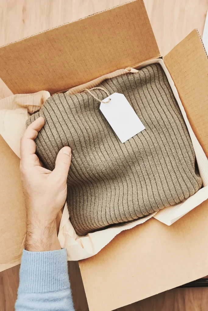 image of hand holding clothing in a box for selling clothes on Etsy
